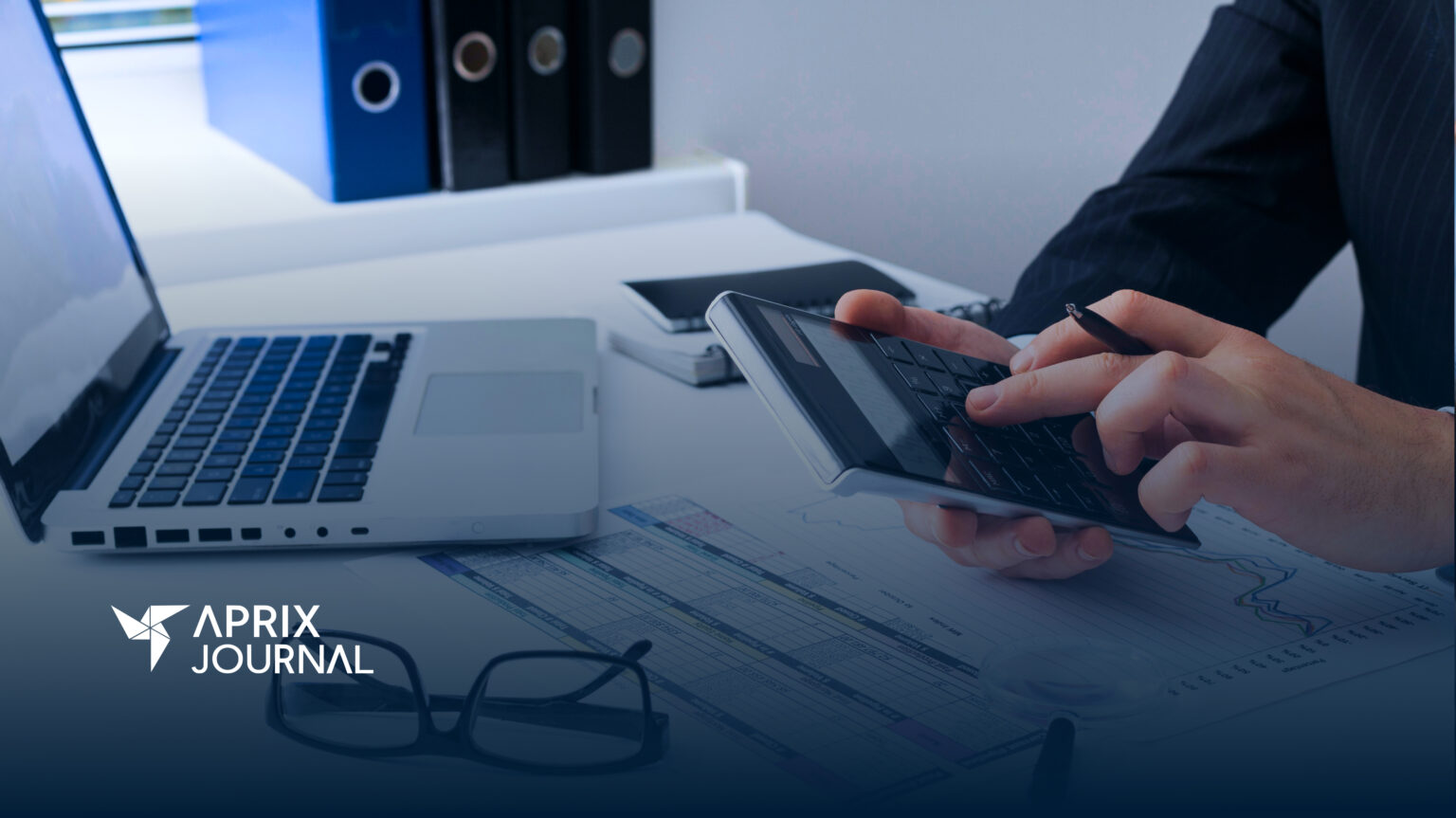 Persona en traje trabajando en una oficina, utilizando una calculadora y un bolígrafo sobre gráficos financieros, con una computadora portátil abierta al lado. Logotipo de "Aprix Journal" en la esquina inferior izquierda.