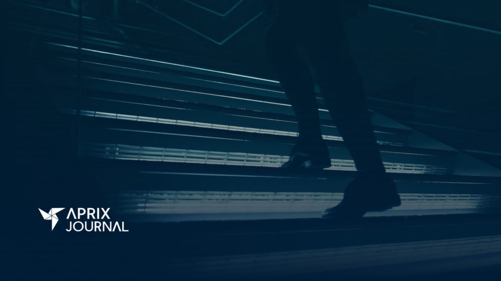 Persona subiendo unas escaleras iluminadas en un entorno moderno, con el logotipo de "Aprix Journal" en la esquina inferior izquierda.